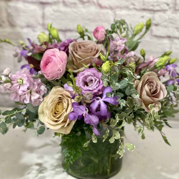 Mixed pink, purple, and beige flowers in a glass vase