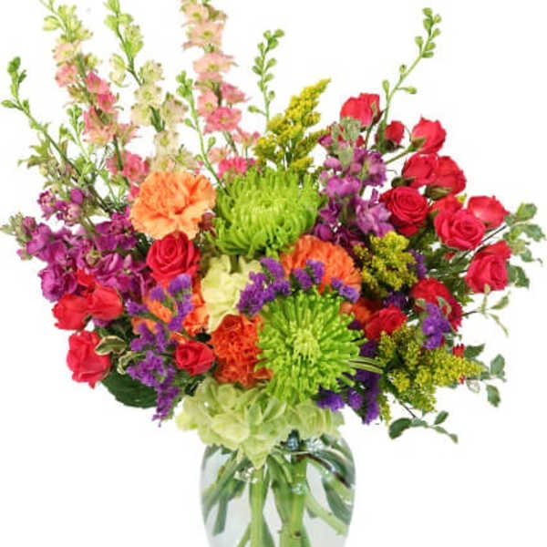 Tall mixed bouquet of bright roses, carnations, mums, and snapdragons in a clear glass vase