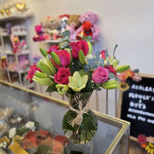 Pink roses and lilies in a clear glass vase with a raffia bow