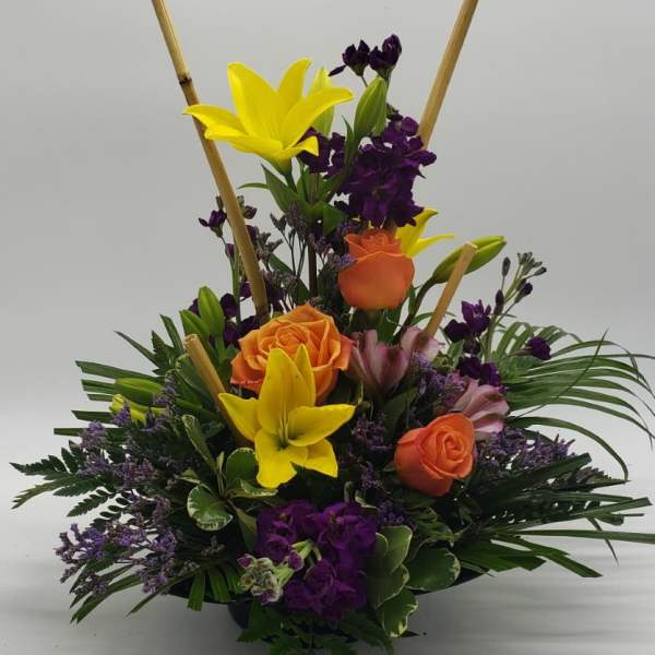 Upright bouquet with yellow lilies, orange roses, and purple flowers