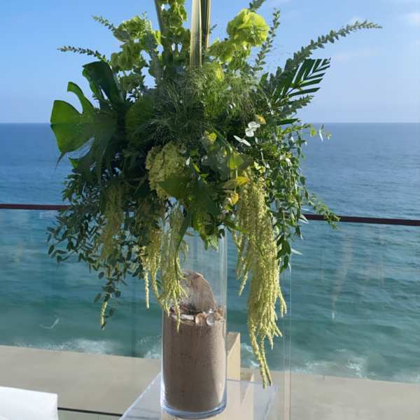 Tall green floral arrangement in a clear vase by the ocean
