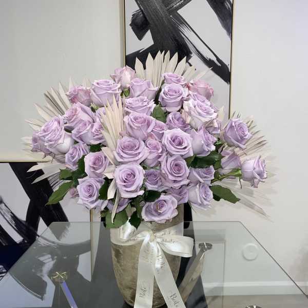 Lavender roses arranged in a vase with pale decorative leaves.