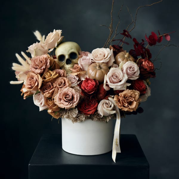 Arrangement of roses with a skull and small pumpkins in a white vase