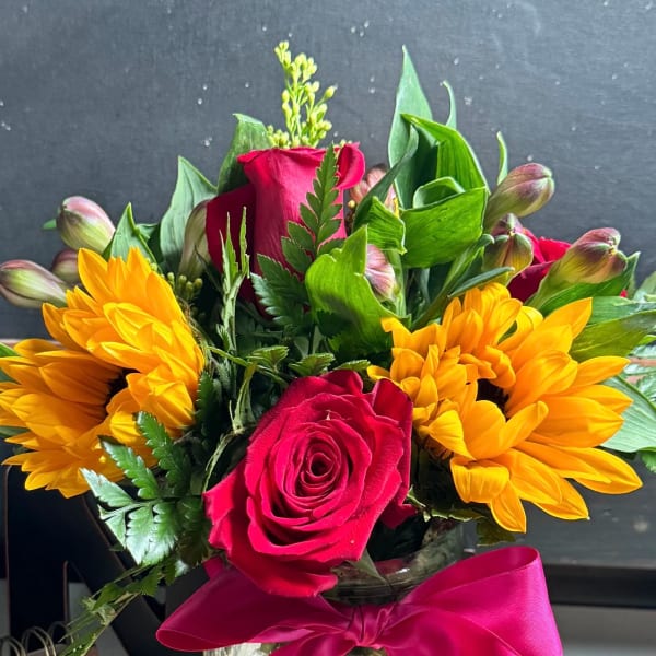 Bouquet of red roses and yellow flowers in a glass jar with a pink ribbon