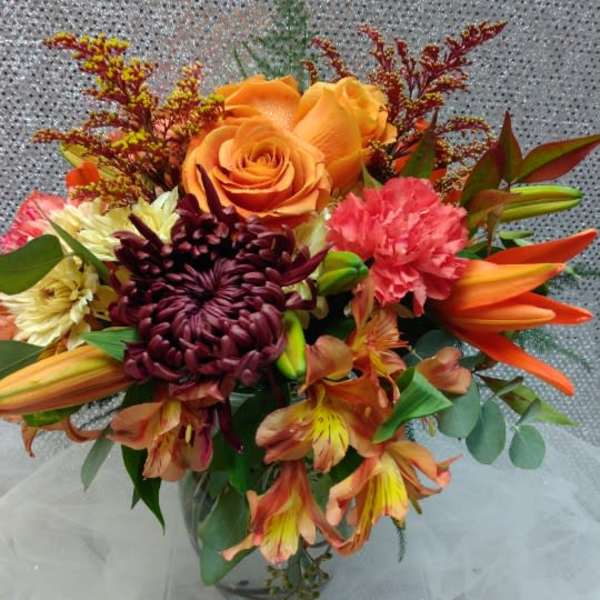 Bouquet of orange roses, lilies, and chrysanthemums in a glass vase