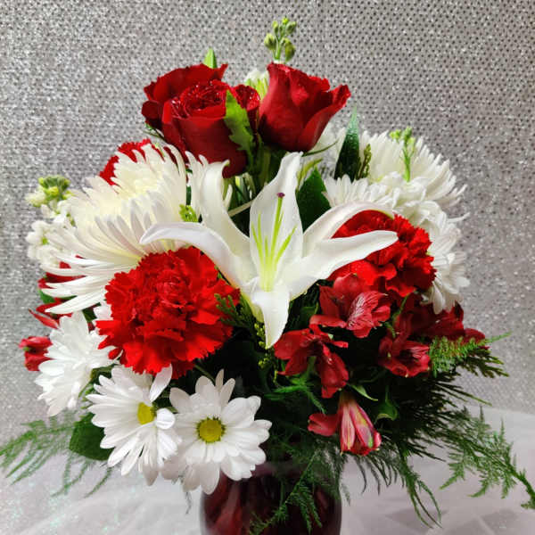 Red roses, white lilies, and daisies in a burgundy vase