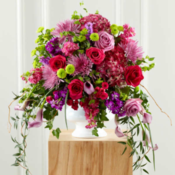 Tall arrangement of pink and red roses, mums, hydrangea and calla lilies in a white pedestal vase