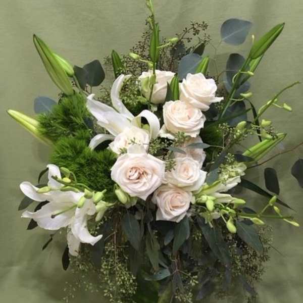White roses and lilies in a glass vase with dark foliage