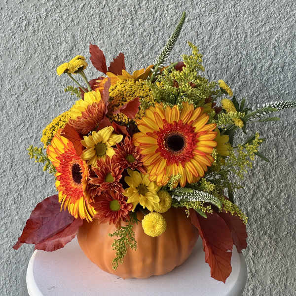Autumn floral arrangement in a pumpkin-shaped container with orange and yellow blooms