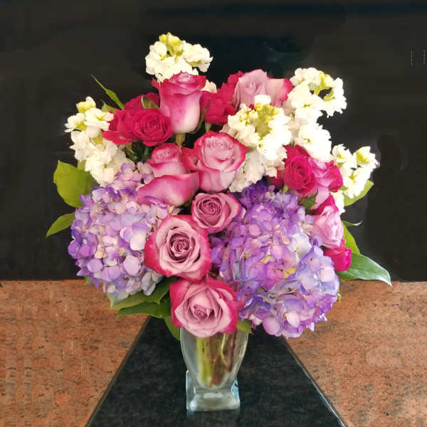 Bouquet of pink roses and purple hydrangeas in a clear glass vase