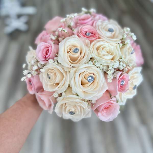 Handheld bouquet of pink and ivory roses with small white filler flowers
