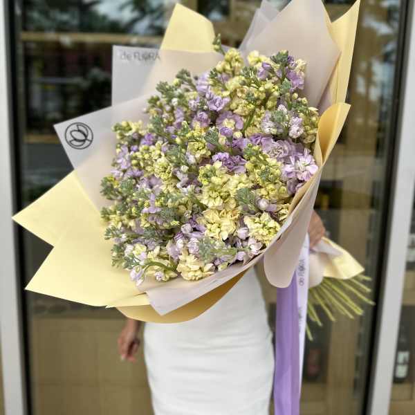 Large bouquet of pale yellow and lavender flowers wrapped in cream paper