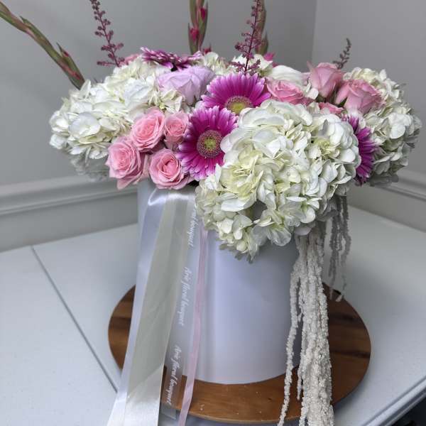 Pink roses and magenta daisies arranged with white hydrangeas in a box
