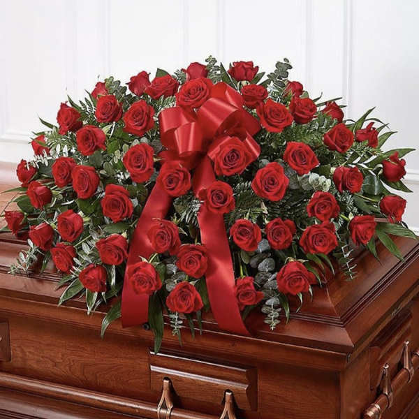 Red rose casket spray with a large red ribbon on a wooden casket