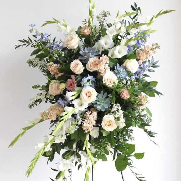 Tall standing spray of white, peach, and blue flowers arranged on a metal easel.