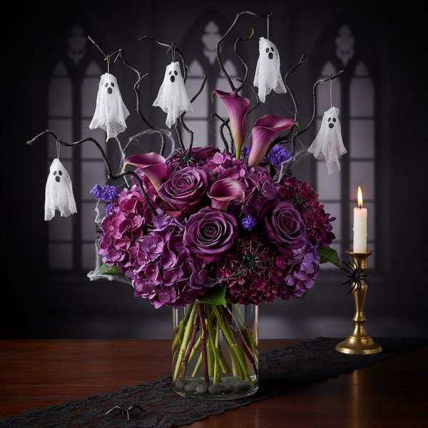 Purple floral arrangement with hanging ghost decorations in a glass vase