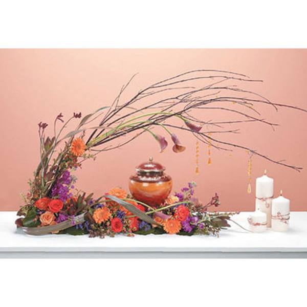 Low floral arrangement with orange and purple blooms beside white candles