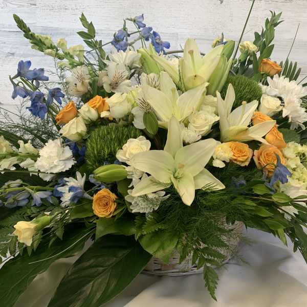 Large mixed floral arrangement with white lilies, orange roses, and blue flowers