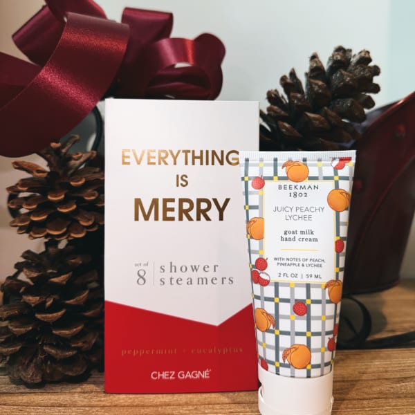 Holiday gift set with shower steamers and hand cream beside pinecones and ribbon