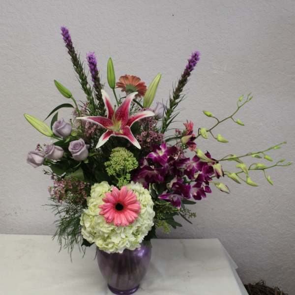 Mixed bouquet in a purple vase with lilies, orchids, roses, and a pink gerbera daisy