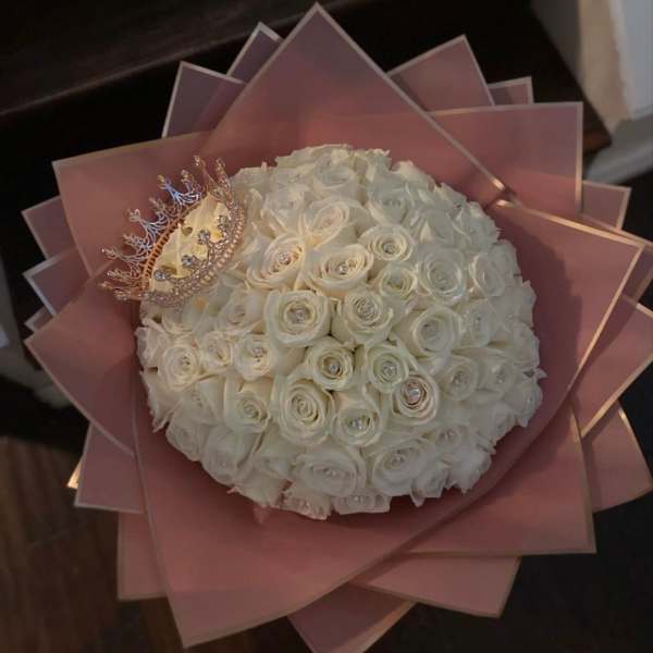 Round bouquet of white roses with a jeweled crown on pink wrapping