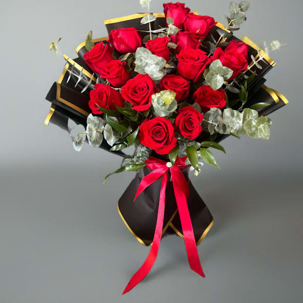 Bouquet of red roses wrapped in black paper with gold trim and a pink ribbon