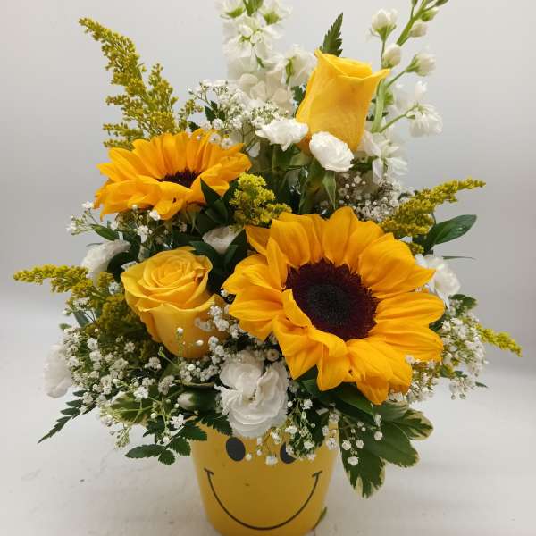 Yellow sunflower and rose arrangement in a smiley-face pot