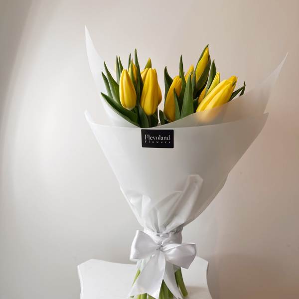 Bouquet of yellow tulips wrapped in white paper with a satin bow