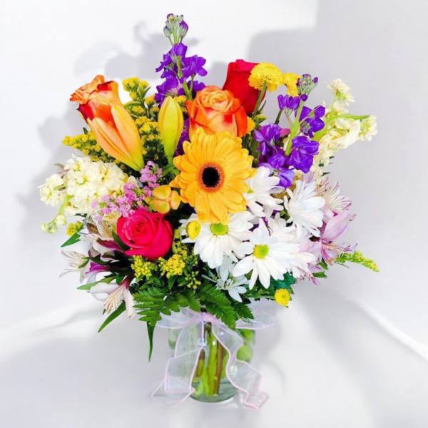 Mixed bouquet of roses, lilies, daisies, and a gerbera in a glass vase