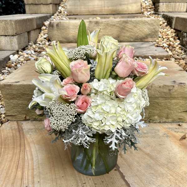 Pink roses and white lilies arranged in a glass vase with white hydrangeas