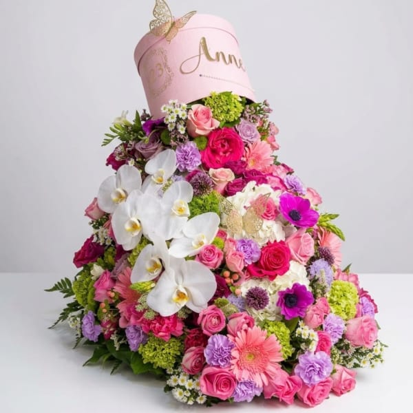 Large pink floral arrangement with white orchids and roses in a pink hatbox
