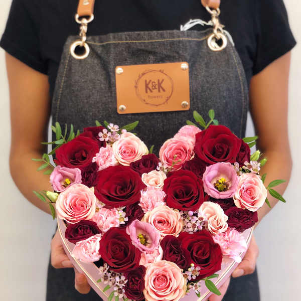Heart-shaped box of red and pink roses held by a person