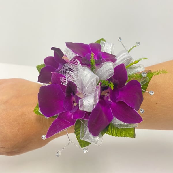 Purple orchid wrist corsage with white ribbon and beads worn on an arm