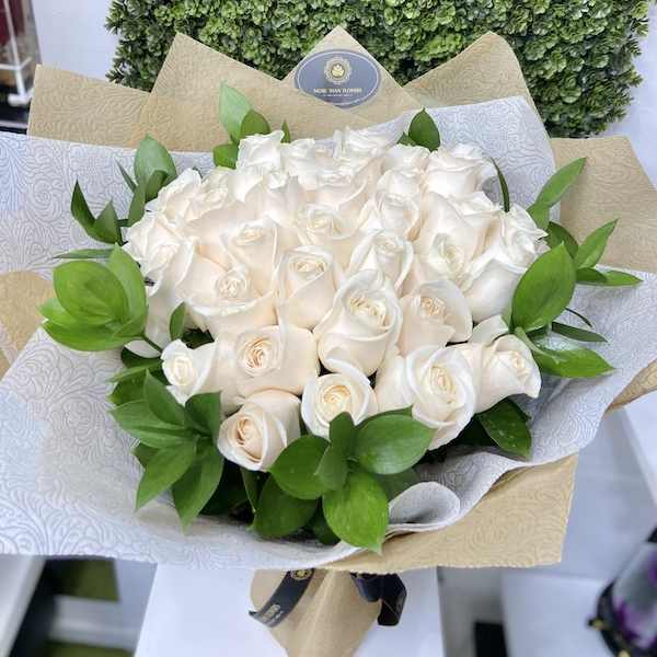 Bouquet of cream-colored roses wrapped in patterned white and kraft paper with a bow.