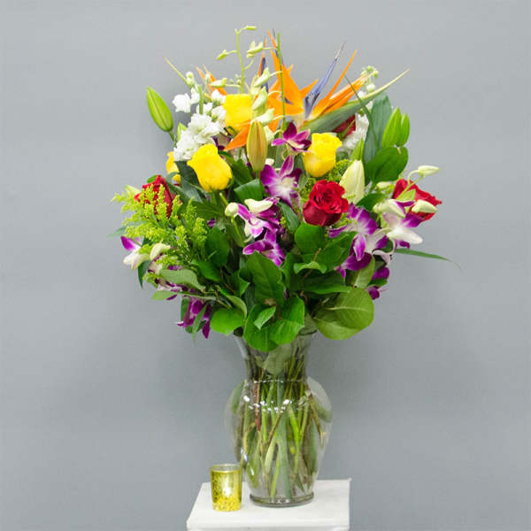 Mixed bouquet of roses, orchids, lilies, and bird of paradise in a glass vase