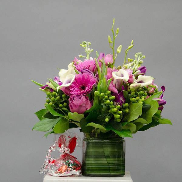 Pink and white mixed bouquet in a glass vase with a small candy bag beside it