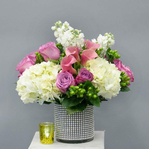 Pink and white floral arrangement in a rhinestone vase with a small yellow candle