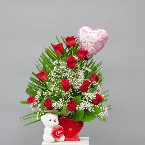 Red roses with a heart balloon and teddy bear in a red container