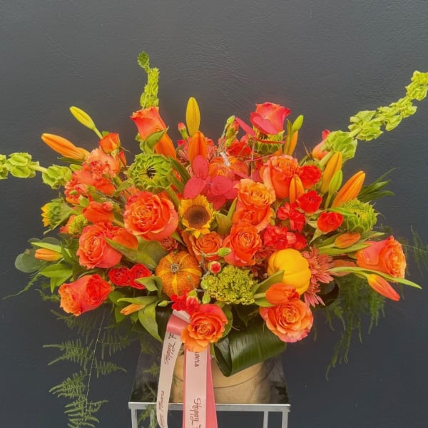Orange and red floral arrangement with roses, lilies, and a small pumpkin accent