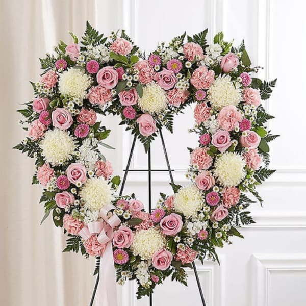 Heart-shaped floral wreath with pink roses and white blooms on a stand