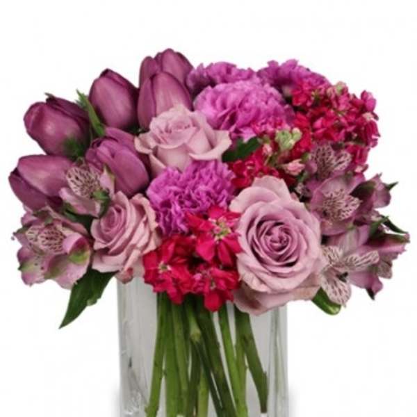 Compact arrangement of pink and purple roses, tulips, and mixed blooms in a clear glass vase