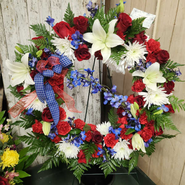 Circular wreath of red, white, and blue flowers on a black stand