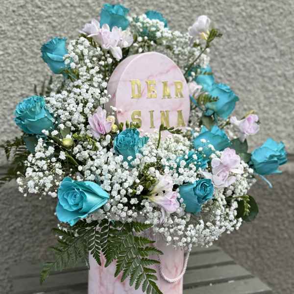 Pink memorial arrangement with blue roses and baby's breath around a name plaque