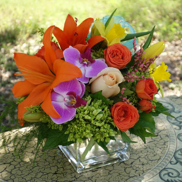 Bright mixed bouquet with orange lilies, roses, and purple orchids in a glass vase