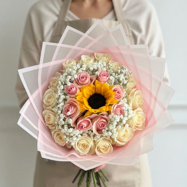 Handheld bouquet of pink and cream roses with a sunflower center