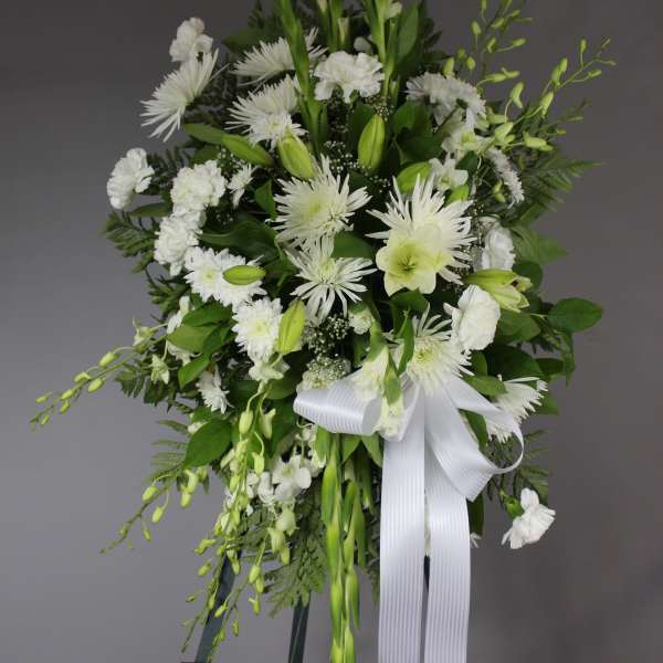 White floral standing spray with a white ribbon on an easel