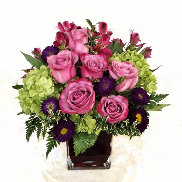 Pink roses and purple flowers in a square glass vase