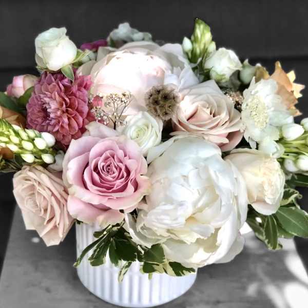 Low arrangement of white peonies, blush roses, and mixed blooms in a white ribbed ceramic vase