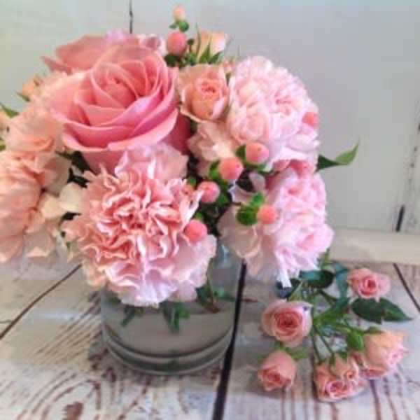 Short glass vase of light pink roses and carnations with extra pink spray roses beside it