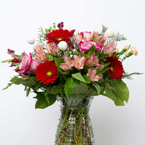 Bouquet of red gerbera daisies and pink flowers in a glass vase
